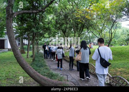 Suzhou, China - June 11, 2024 : A group of people walk along a path in a lush Chinese garden. Stock Photo