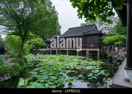 Suzhou, China - June 11, 2024 : A traditional Chinese garden in Suzhou with a wooden pavilion overlooking a pond filled with lily pads. Stock Photo