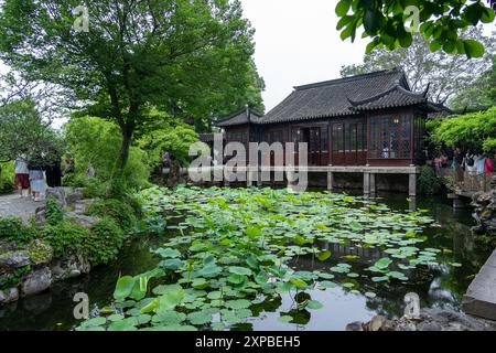 Suzhou, China - June 11, 2024 : A pond in a Chinese garden with a wooden pavilion, lush foliage, and stone paths. Stock Photo