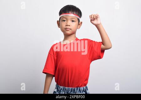 Cheerful Asian boy in red t-shirt raising his hand in air with happy and successful expression, isolated on white background. Indonesian Independence Stock Photo