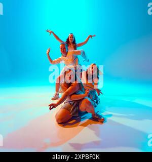 Group of female dancers in retro casual attire posing perform bold and creative poses in vibrant neon light against gradient studio background. Stock Photo