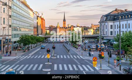 Vasagatan, Vasa Street, evening light, the old town of Stockholm in the distance. Tourist and locals walking, trails of cars passing by Stock Photo