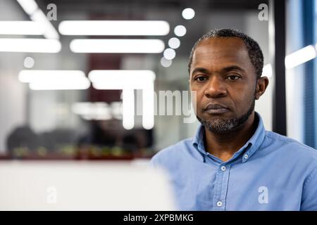 Professional man focused on task working on laptop in modern office setting. Intense expression showing concentration and dedication. Bright office lighting. Technology and productivity concepts. Stock Photo