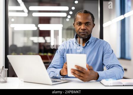 Business professional using tablet and laptop in modern office. Focused on work, multitasking, checking information. Ideal for business, technology, office professions, productivity concepts Stock Photo