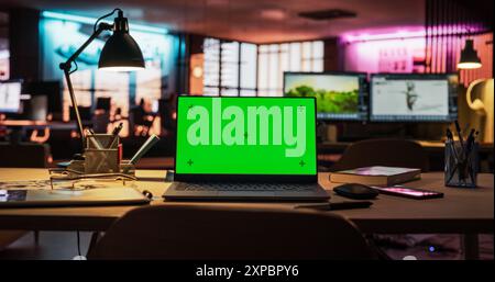 Laptop Computer Standing on a Wooden Desk with a Green Screen Chromakey Mock Up Display. Creative Office Working Station for Game Developer and Graphic Designer in Creative Agency Stock Photo