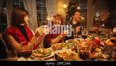 Family and Friends Gather at Home for a Traditional Christmas Dinner with a Turkey Roast Feast. Happy Successful People Celebrating Holiday, Singing Christmas Carols Together and Holding Sparkles Stock Photo