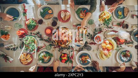 Diverse Group of Relatives and Friends Sitting Together Behind a Dining Table with Tasty Meals and Festive Decorations. People Sharing Food, Talking, Creating Joyful Holiday Atmosphere. Top Down View Stock Photo