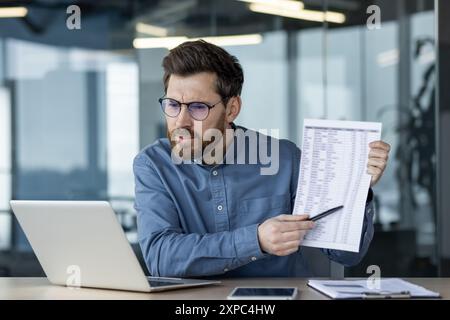Businessman in virtual meeting showing document and explaining data during online conference. Professional working from modern office, discussing report on laptop, using technology Stock Photo