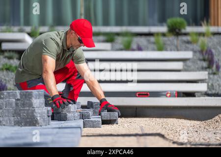A worker is carefully placing pavers in a contemporary outdoor space while wearing safety gloves and sunglasses. Stock Photo
