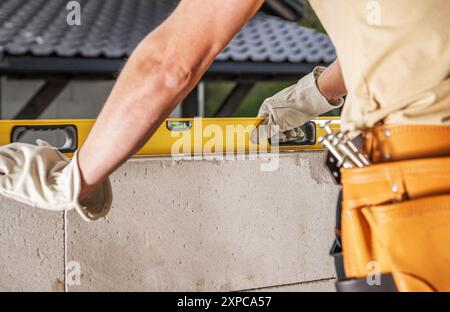 A construction worker checks the level of a block wall using a leveling tool at a building site. Stock Photo