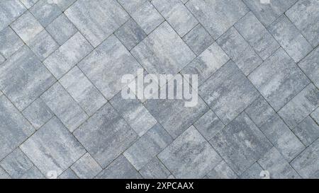 A close-up view of a gray paved surface arranged in a herringbone pattern, showcasing its textured design and color variations. Stock Photo
