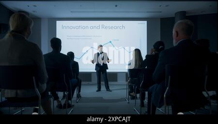Corporate Event: Caucasian Male Tech CEO Giving Presentation To Colleagues or Investors In the Conference Room Of Innovative Startup Office. Man Talking About Business Objectives and Profit Margins. Stock Photo
