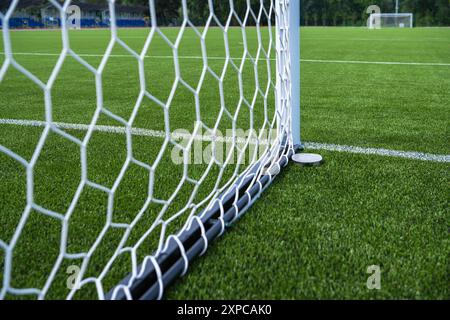 The close-up view of a soccer goal net against a vibrant green turf field under clear skies. Stock Photo