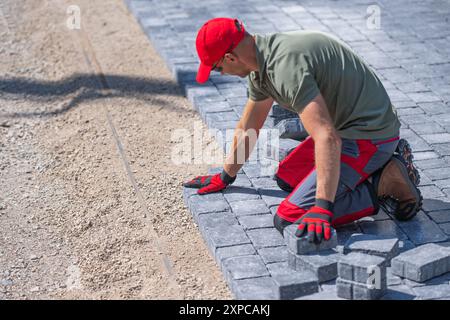A worker is carefully laying down pavers on a prepared gravel base, focusing on alignment and precision. Stock Photo