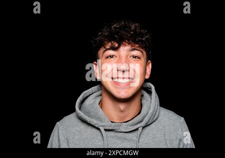 Portrait of a smiling Caucasian man in his 20s wearing a sweatshirt against a dark background. Stock Photo