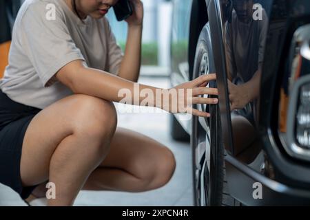 A young woman is checking the condition of her car's tires Stock Photo