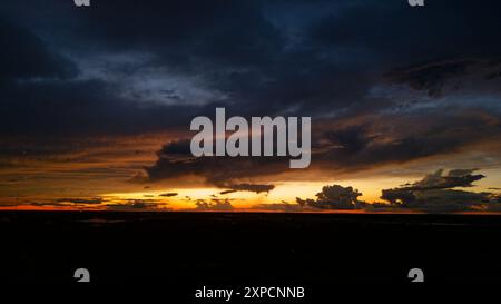 Bright colorful intense light from the sun setting and the dark clouds on the horizon after a severe thunderstorm at night Stock Photo
