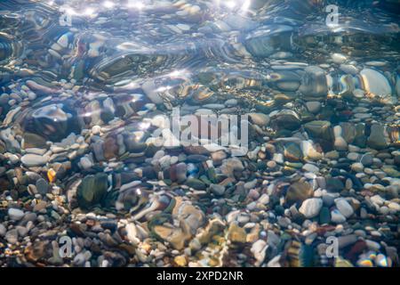 multi-colored stones under water on the sea, river. Natural background of stones, glare on the water Stock Photo