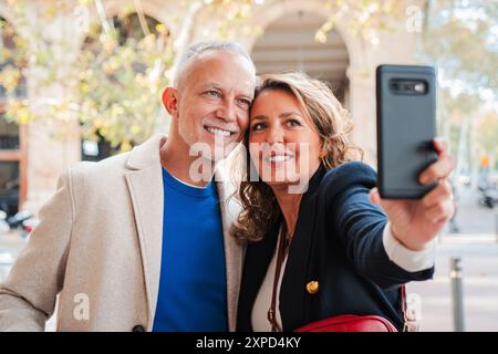 Married mature couple smiling and having fun taking a selfie with a callphone during a vacation trip. Middle-aged man and woman enjoying while sightseeing and shooting a photo with a mobile phone. High quality photo Stock Photo