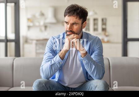 Thoughtful Man Sitting on Couch in Living Room Stock Photo