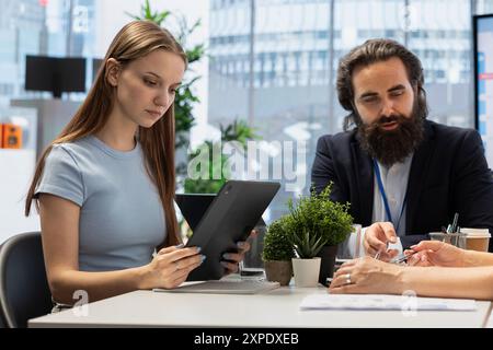 Portfolio Manager in office meeting analyzing economic reports, discussing with gen Z girl wanting to invest. Financial advisor helping young adult looking to increase wealth Stock Photo