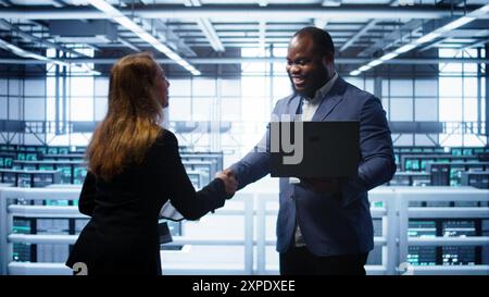 African american admin greeting inspector arriving in data center to supervise operations. IT expert in server hub workspace doing hand shake with supervisor monitoring performance, camera B Stock Photo