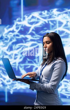 Software engineer solving tasks on laptop, running artificial intelligence programming scripts. Woman in modern lab using notebook to write lines of code for AI applications development Stock Photo