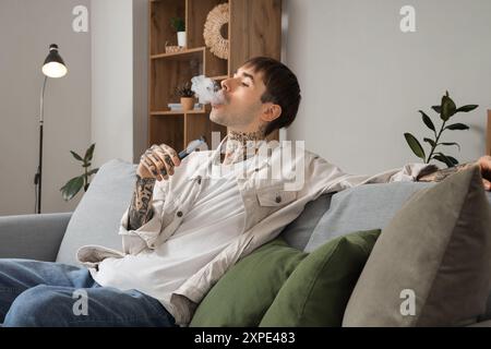 Young man smoking disposable electronic cigarette at home Stock Photo