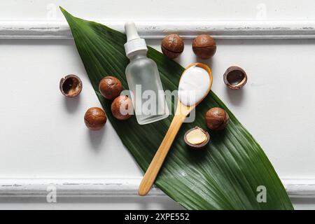 Macadamia nuts, green leaf, wooden spoon and bottle of cosmetic product on white background Stock Photo