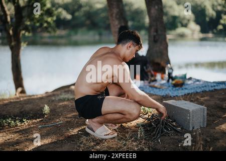Young man preparing a barbeque fire during a scenic mountain picnic by the lake Stock Photo