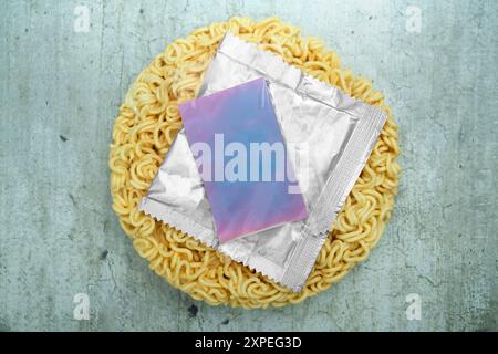 A package of ramen noodles sits on a table next to a packet of sauce and a packet of plastic wrap Stock Photo