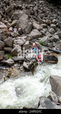 A single adult women crossing a tyrolean  traverse suspended above Boulder Creek in Boulder Canyon, Boulder , Colorado Stock Photo