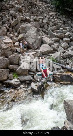 A single adult women crossing a tyrolean  traverse suspended above Boulder Creek in Boulder Canyon, Boulder , Colorado Stock Photo