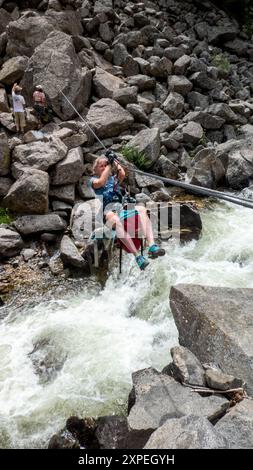 A single adult women crossing a tyrolean  traverse suspended above Boulder Creek in Boulder Canyon, Boulder , Colorado Stock Photo