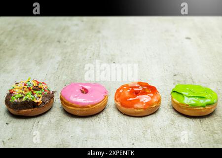 Four donuts with different colors and flavors. The donuts are arranged in a row on a table Stock Photo