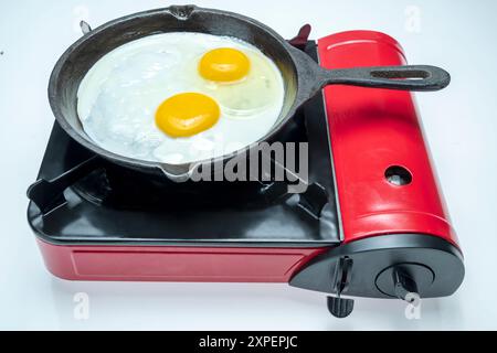 A red pan with a yellow egg in it sits on top of a red stove. The stove is a portable one, and the pan is made of iron. Concept of warmth and comfort, Stock Photo