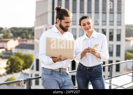 Young professionals collaborating on rooftop with laptop and phone Stock Photo