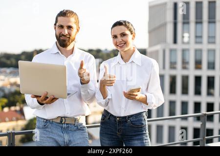 Happy professionals collaborating on rooftop with laptop and phone Stock Photo