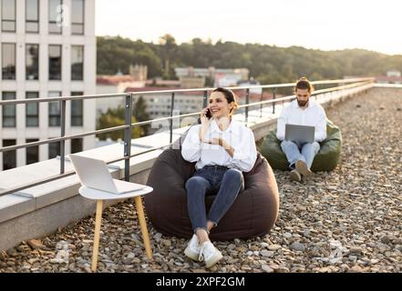 Young professionals working remotely on rooftop with laptops Stock Photo