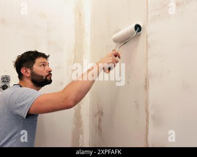home improvement. Caucaisan man applying wall treatment, putting up glue for wallpaper using construction roller Stock Photo
