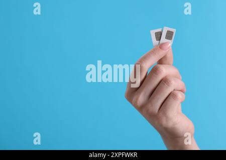Woman holding SIM cards on light blue background, closeup. Space for text Stock Photo
