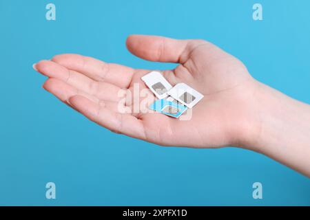 Woman holding SIM cards on light blue background, closeup Stock Photo
