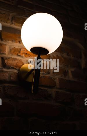 Classic bra lamp on brick wall. Light in the darkness. Interior electricity. Wall lantern with warm light on the wall. Illumination concept. Stock Photo