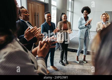 Diverse group of people standing in a circle, clapping and smiling during a seminar. The atmosphere is positive and collaborative. Stock Photo