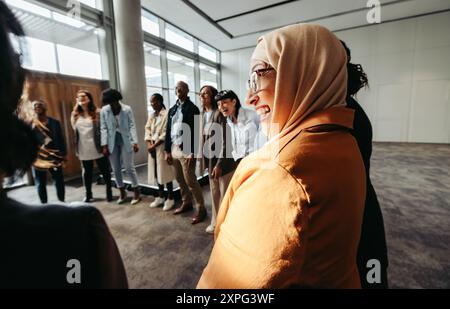 A diverse team engages in a bonding activity, with a Muslim woman laughing in a circle during a workshop. Stock Photo