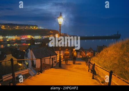 People walking down the famous 199 steps at night to Whitby old town with view of the river esk, harbour and pier, North Yorkshire coast, England, UK Stock Photo