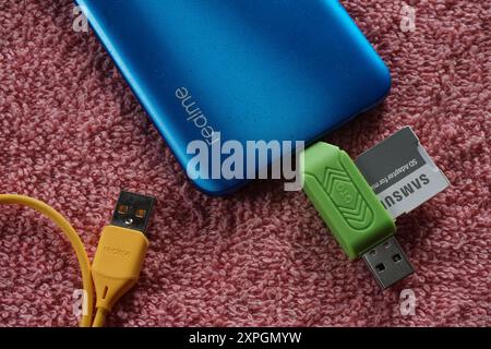 Terengganu, Malaysia - 24 August 2024 : Closeup of otg flash drive, samsung sd adapter, yellow realme cable and realme smartphone on red backgrouund. Stock Photo