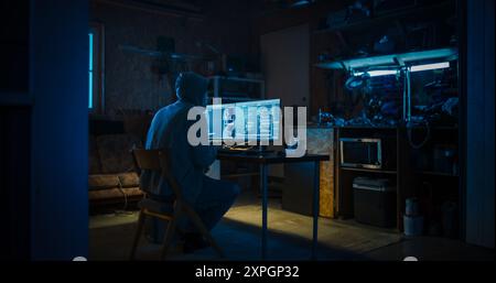 Backview Of Anonymous Professional Programmer Obsessively Writing a Code on His Desktop Computer, Late at Night In Garage. IT Specialist Ethical Hacker Working on Finding Software Vulnerabilities. Stock Photo