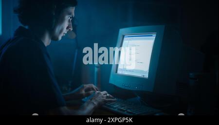 Caucasian Male Web Designer Using Old Desktop Computer In Retro Garage Late At Night. Focused Internet Enthusiast Writing Code At Home. Programming Successful Social Network Website In Nineties. Stock Photo