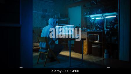 Backview Of Anonymous Professional Programmer Obsessively Writing a Code on His Desktop Computer, Late at Night In Garage. IT Specialist Ethical Hacker Working on Finding Software Vulnerabilities. Stock Photo